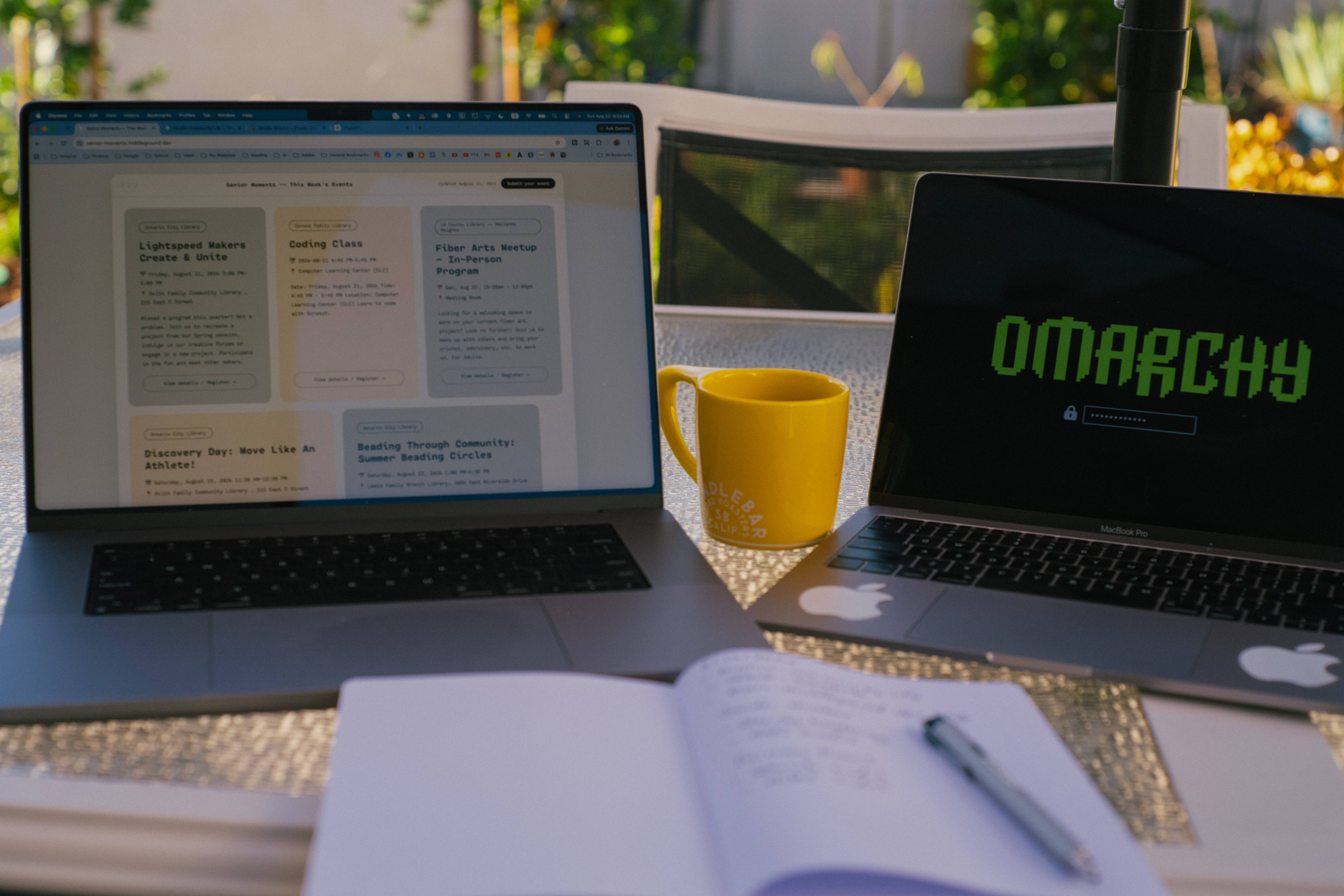 Two laptops, a yellow mug, and a notebook on the patio, one screen showing Omarchy